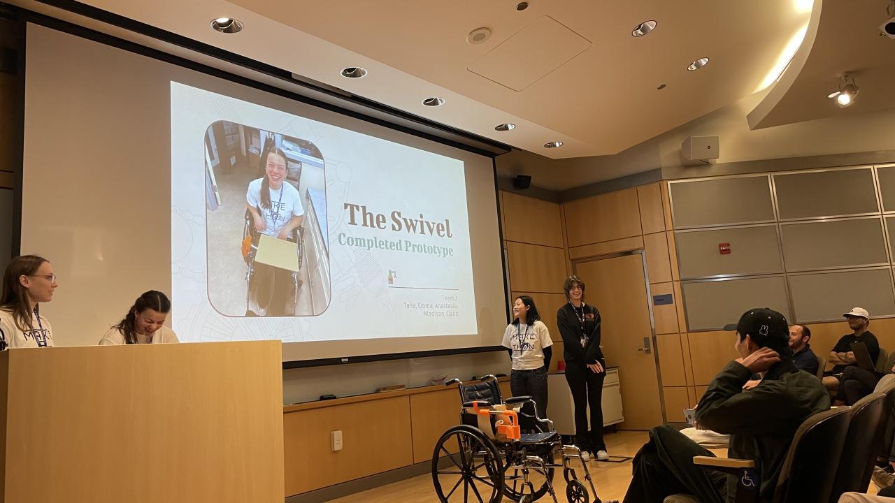 A group presents "The Swivel Completed Prototype" in a lecture hall; a slide shows a person using the device and a wheelchair with an attached tray is displayed in front.